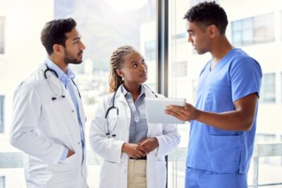 Healthcare professionals discussing patient data on tablet in hospital corridor