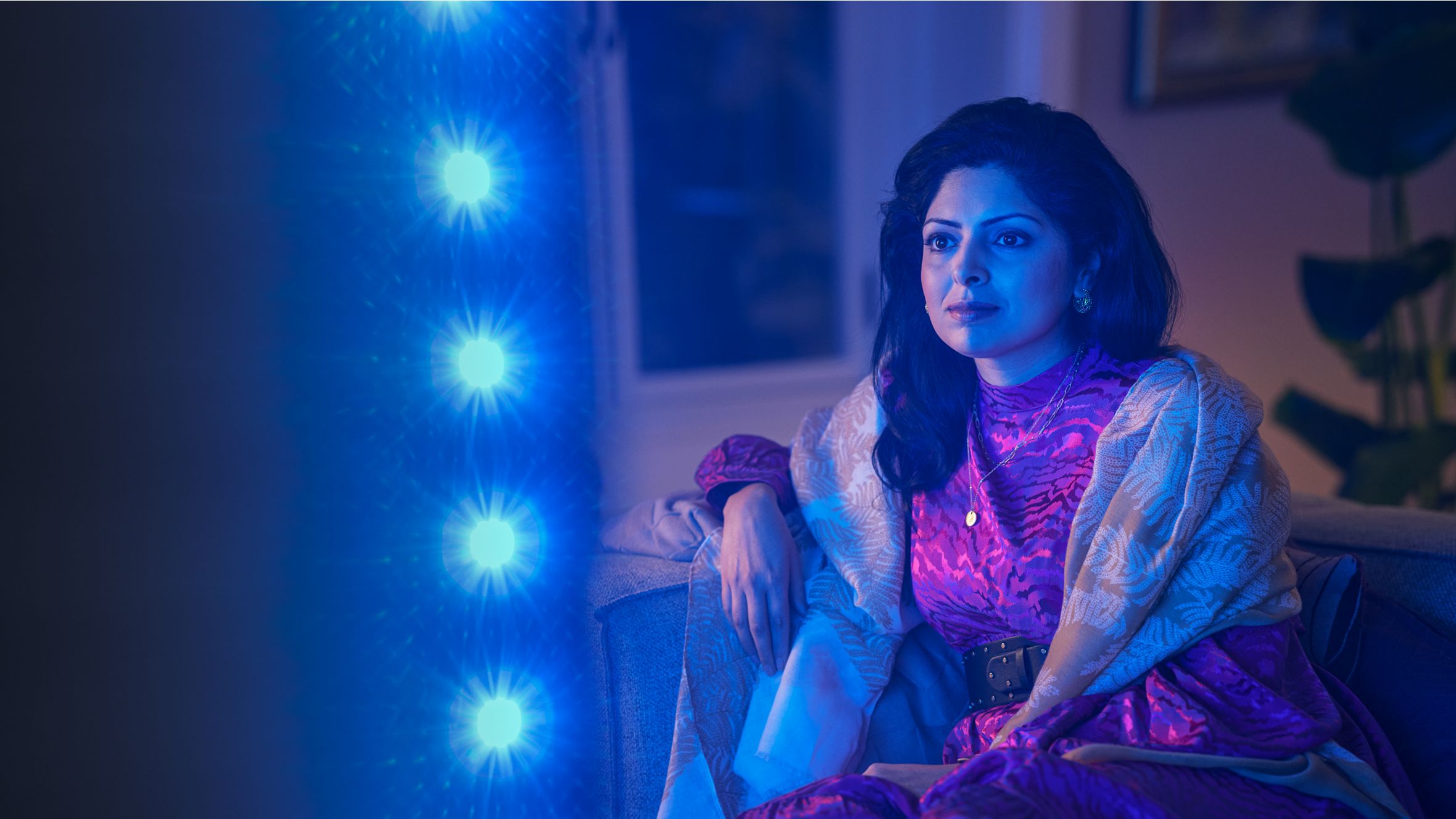 Woman watching a Philips Ambilight TV, with blue ambient light reflecting beside the screen.