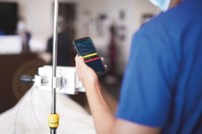 Un profesional médico revisa los signos vitales del paciente en una aplicación móvil de monitorización de pacientes de Philips junto a la cama