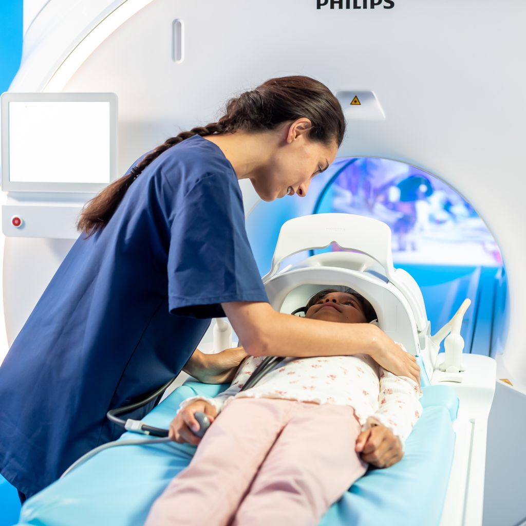 Girl lying on MRI bed, before the MRI procedure with In-bore Connect and technician reassuring.