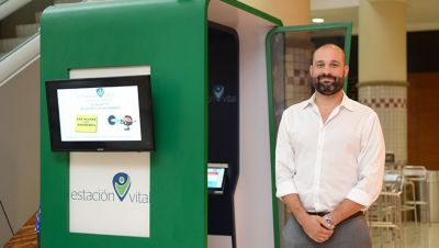 Man standing next to Estación Vital health screening booth in public space
