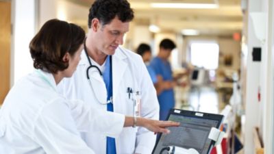 Doctors reviewing patient data on tablet in hospital corridor
