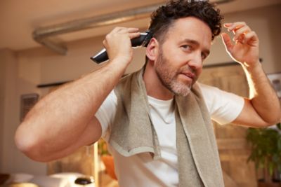 Ein Mann schaut in die Kamera, w&auml;hrend er einen Philips Haarschneider verwendet, um seine Haare zu schneiden.