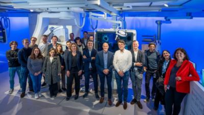 Een groep professionals staat in een ruimte voor beeldgestuurde therapie met een Philips Azurion-systeem onder blauwe verlichting