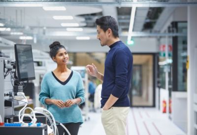 Two Philips employees discussing work near medical equipment in a modern research and innovation facility