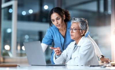 Two clinicians reviewing cardiac monitoring data on laptop in hospital setting