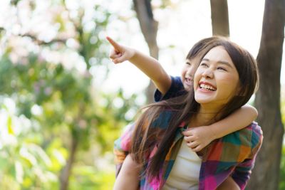  Mère portant son enfant sur son dos, souriant dans un parc pendant que l’enfant pointe devant lui