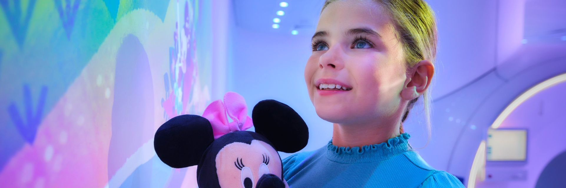 Girl with Minnie doll looking at Ambient Experience with Disney theme prior to MR exam