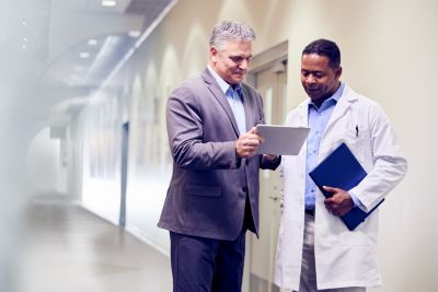 Profissional de saúde e colega analisando informações em um tablet no corredor de um hospital
