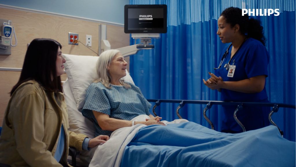 Older woman sits in emergency department bed speaking with clinician and awaiting ECG test.