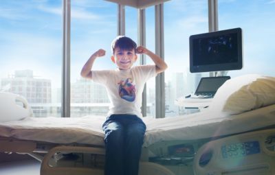 Child sitting on hospital bed smiling during heart health awareness campaign