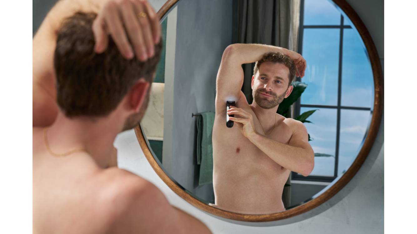 Ein Mann rasiert sich vor dem Badezimmerspiegel mit dem Philips Bodygroom die Achseln.