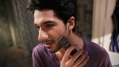 Un joven con camiseta morada se afeita el borde recto de las patillas con una recortadora de barba Philips.
