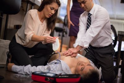女性がAEDパッドを準備している間、心肺蘇生を行う男性