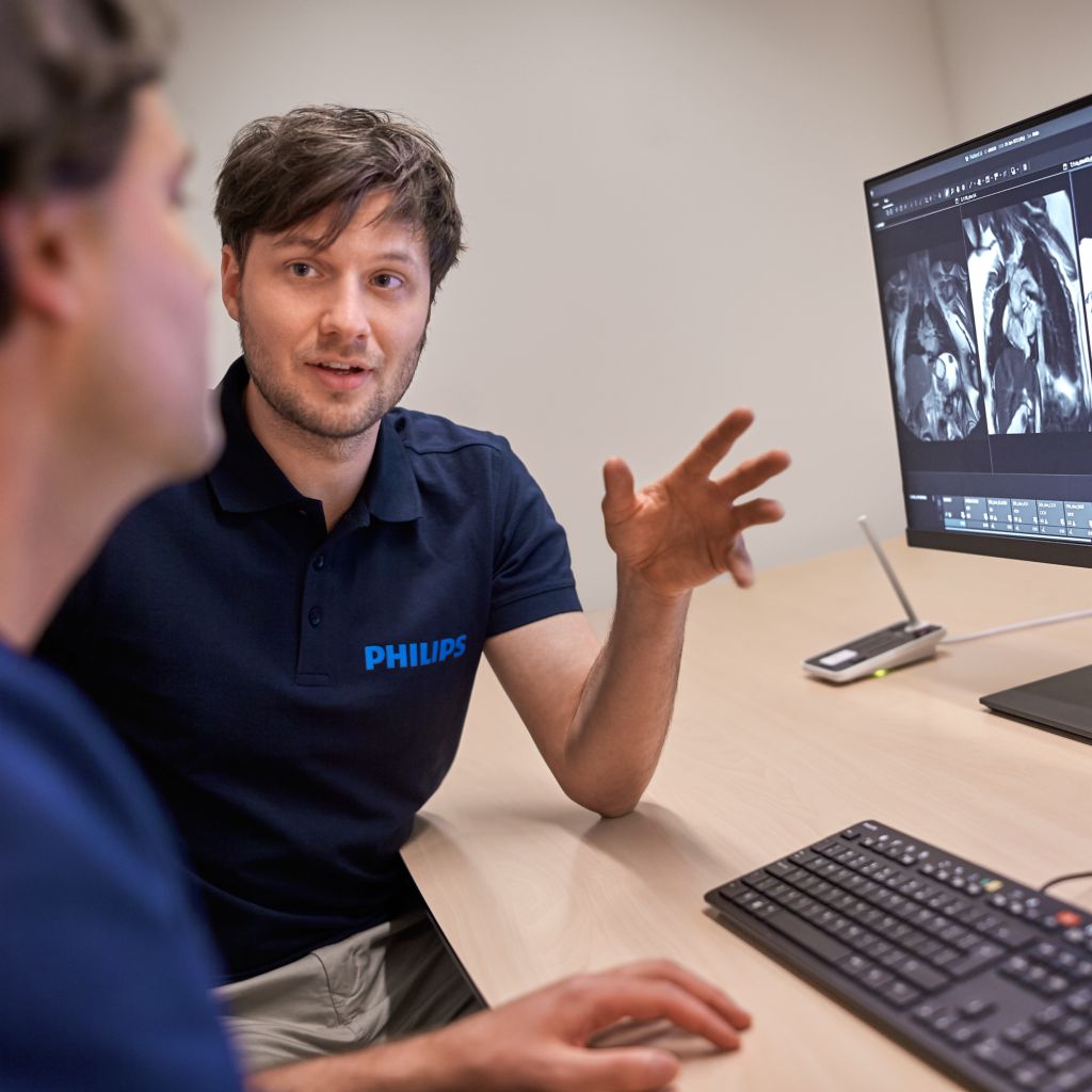 Philips clinical advisor talking to an MR technologist sitting behind the MR console