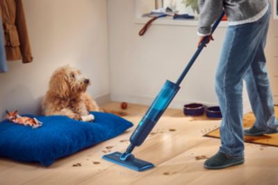 Person cleaning floor with electric mop near pet