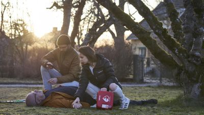 Två personer hjälper en man som ligger på marken med en Philips-AED utomhus.