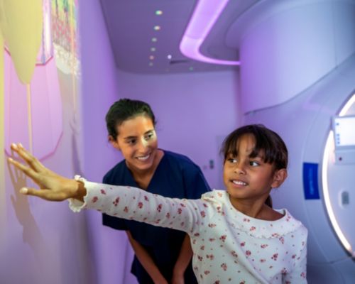 Un enfant accompagné d’une manipulatrice en électroradiologie médicale joue avec l’univers Ollie d’Ambient Experience projeté sur un mur, avant un examen IRM