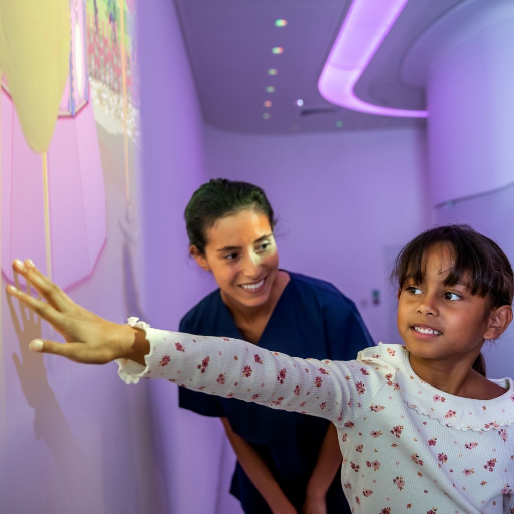 Child playing with Ambient Expeirence Ollie theme on wall guided by technician prior to an MRI exam