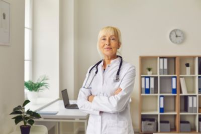 Pracownik ochrony zdrowia w białym fartuchu stoi w dobrze oświetlonym gabinecie klinicznym