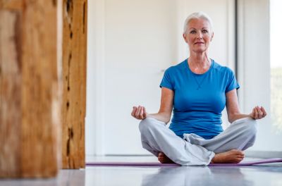 Senior woman sitting cross legged on yoga mat practicing meditation indoors