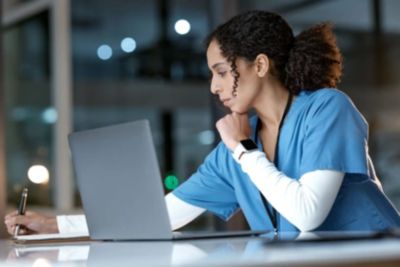 Enfermeira trabalha no laptop revisando informações do paciente em ambiente clínico