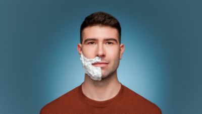 Um homem com espuma de barbear num lado do rosto olha diretamente para a c&acirc;mara.