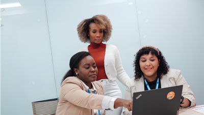 Three women collaborating over a laptop in a meeting room