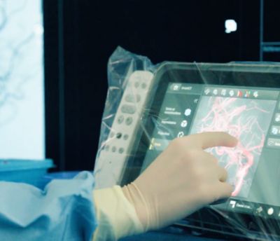 Interventional neuroradiologist manipulating bedside touchpad in interventional suite