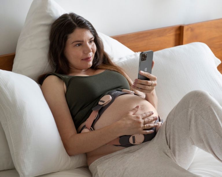 Woman lying on bed with fetal monitor on, looking at her phone