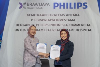 Astri Ramayanti Dharmawan dan Amira Ganis berjabat tangan sambil memegang MoU yang telah ditandatangani