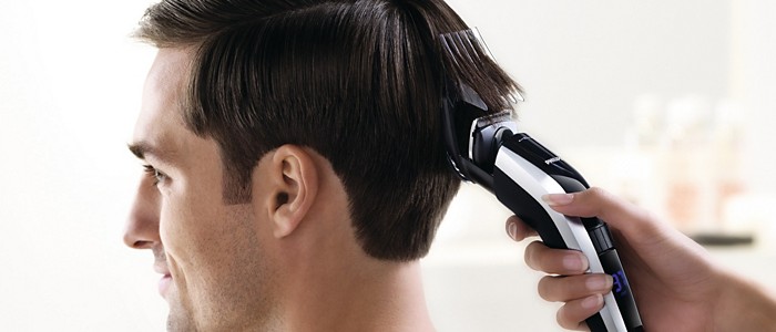 A woman using a Philips hair clipper to shave a man’s dark hair into a mullet.