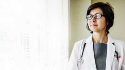 Doctor wearing glasses and white coat looking out of a window