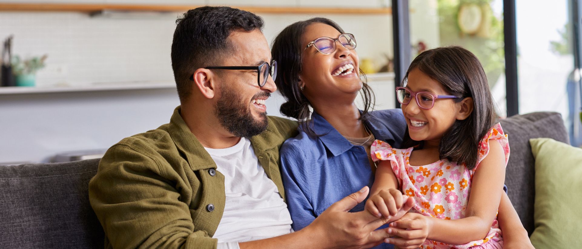 Family with mother, father and young daughter sitting on couch smiling.