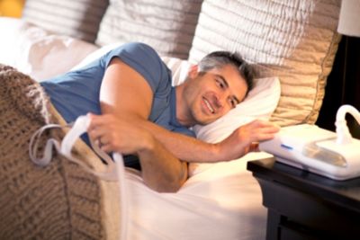 Man in bed operating CPAP on bedside table 