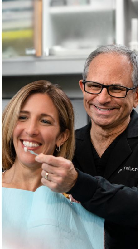 A dental professional checks the shade of a patient's tooth.