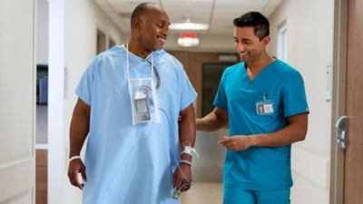 Clinician walking with cardiac patient wearing portable telemetry monitor in hospital hallway