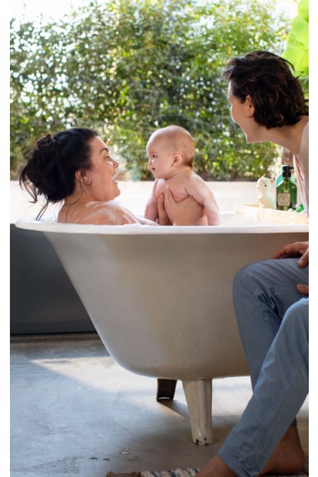 Baby smiling in a bath with two women