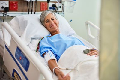 female patient smiling in hospital bed with SpO2 glove sensor, non-invasive blood pressure cuff, and ECG leads