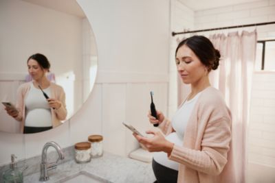A pregnant woman checking her brushing behaviors on an app, while holding a toothbrush in her other hand