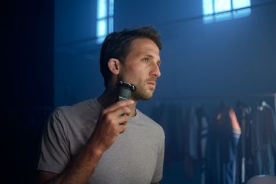 Hombre utilizando una afeitadora rotativa de afeitar frente al espejo. T&eacute;cnica perfecta para un afeitado apurado en seco.