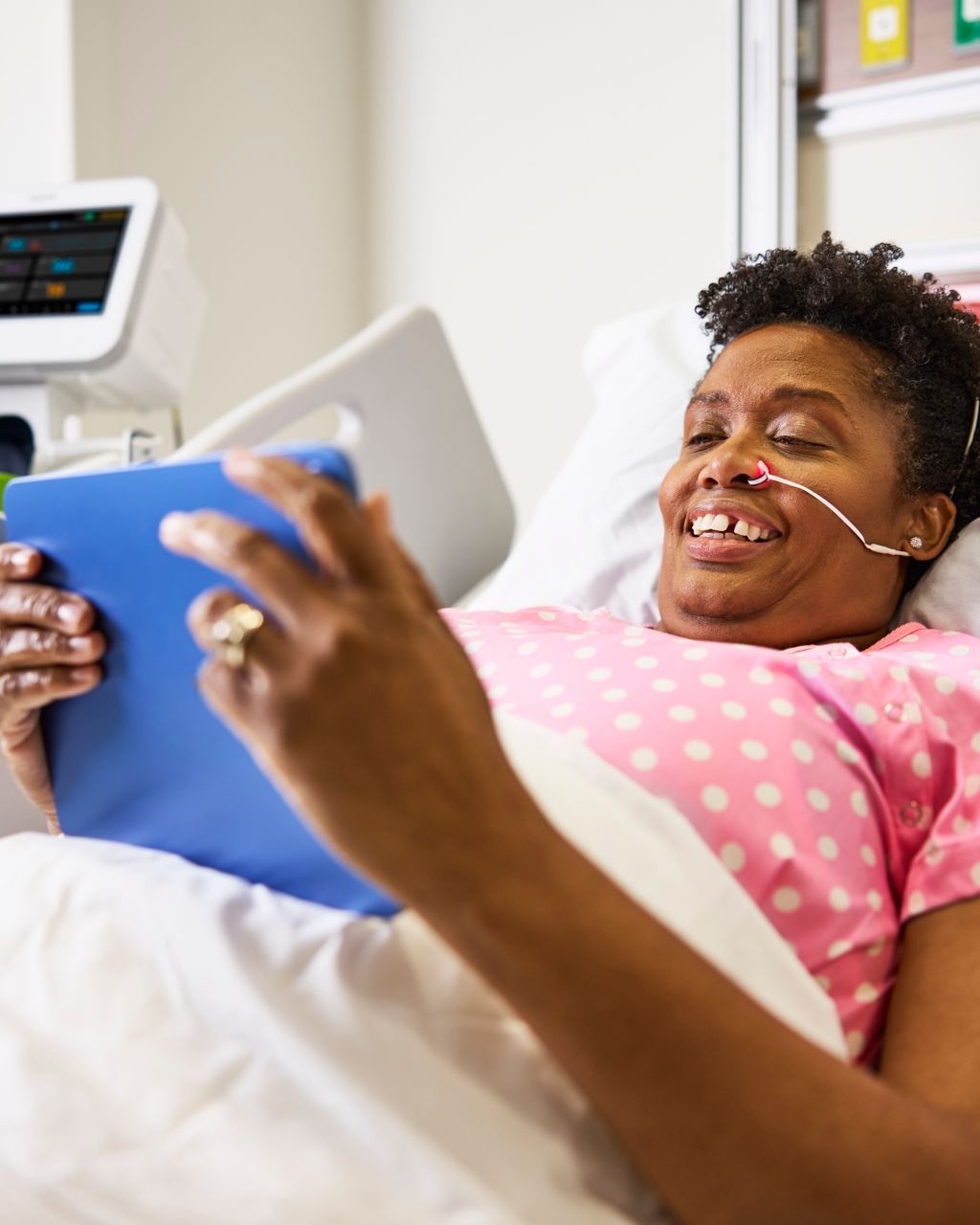 Femme alitée à l’hôpital portant le capteur de SpO₂ nasal Alar et tenant une tablette