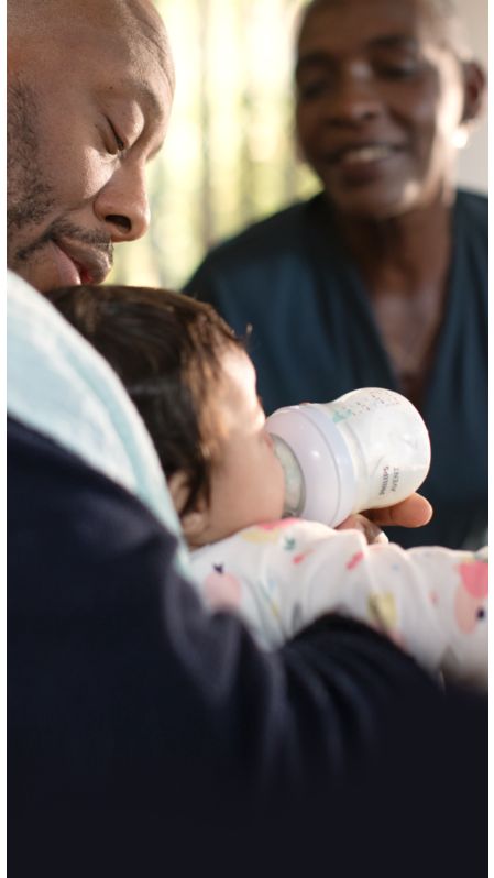 Un padre da el biberón a un bebé, biberón Natural Response de Philips Avent