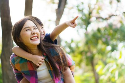 Mother carrying child on her back smiling in park while child points ahead