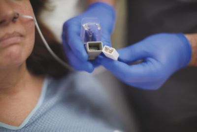 Intensivvårdspatient med alarmsensor medan en kliniker håller i en anslutning