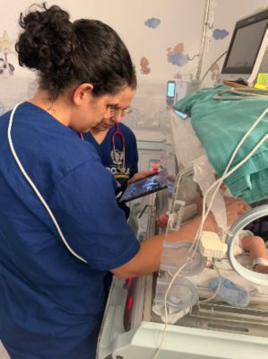 A healthcare professional uses a tablet beside an infant in an incubator.