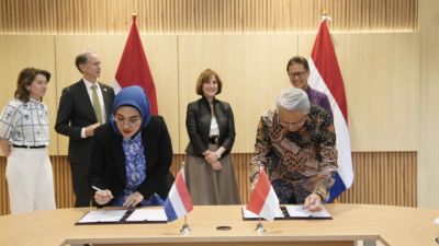 Astri R. Dharmawan and Kunta Wibawa Dasa Nugraha sign the MoU in front of Indonesian and Dutch flags.
