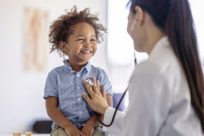 Pediatrician listening to young child’s chest during clinic visit