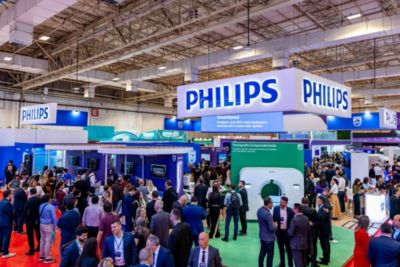 Estande da Philips na JPR 2024 exibindo tomógrafo e soluções de IA para radiologia com visitantes explorando tecnologias