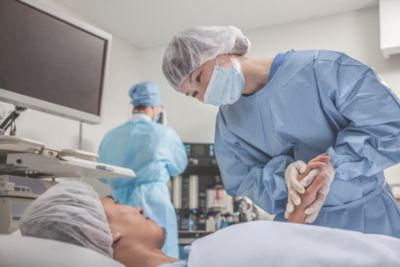 一名临床医生在手术室中协助患者，另一名临床医生则在调整麻醉和监测设备